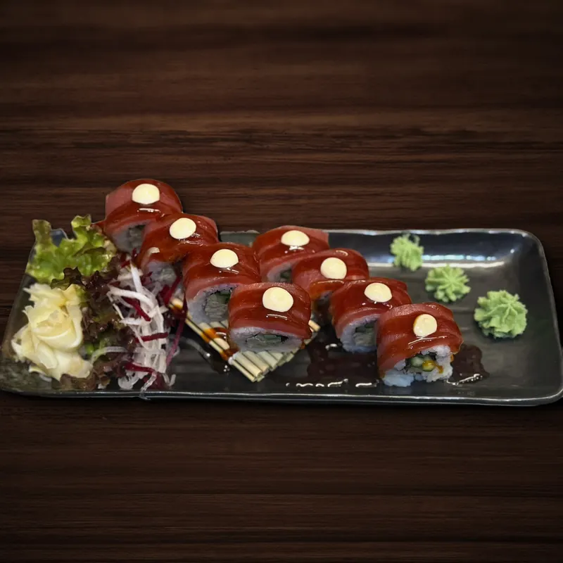Acht Sushi-Rollen-Stücke, umhüllt von Thunfisch mit glänzender dunkler Soße und je einem Klecks heller Soße, auf einem schwarzen Teller mit eingelegtem Ingwer, Salat, Rettichstreifen und Wasabi.