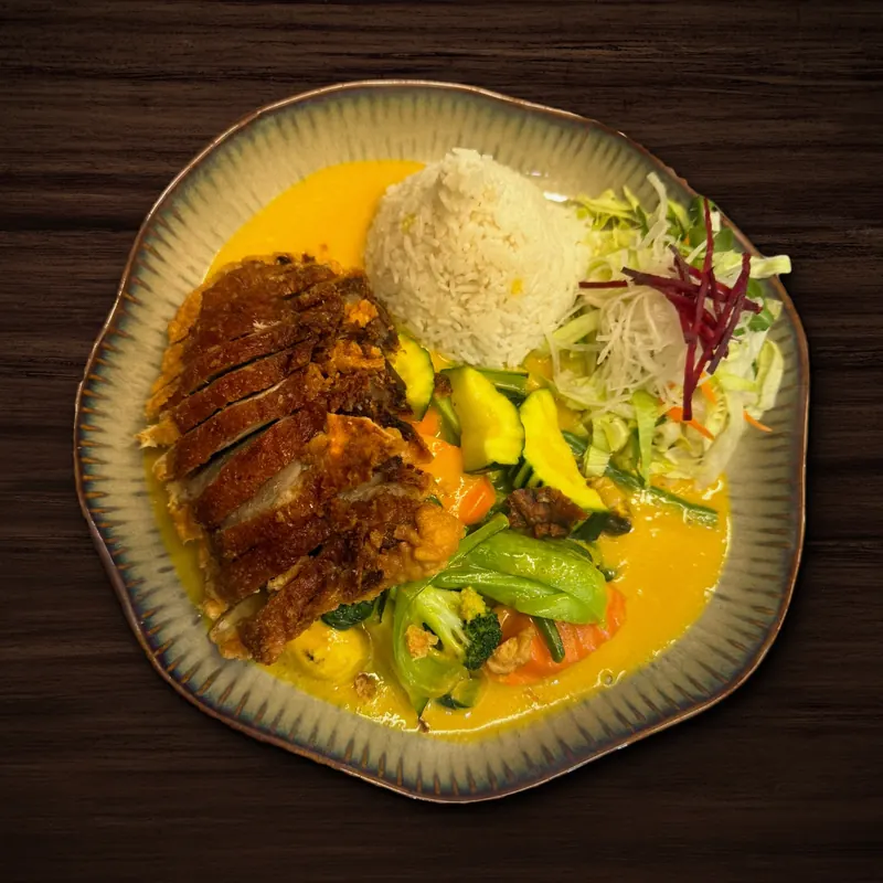 Knusprig paniertes, in Scheiben geschnittenes Fleisch mit Wokgemüse wie Zucchini, Karotten, Pak Choi und Brokkoli in gelber, cremiger Soße, dazu ein Reisberg und etwas Salat mit Rote-Bete-Streifen.